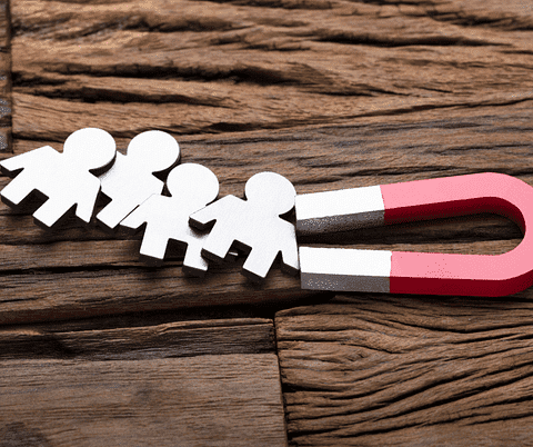 A red and white horseshoe magnet pulls four paper cut-out people, highlighting the attraction of a hyperlocal digital marketing agency in Pune. - IPSense.com
